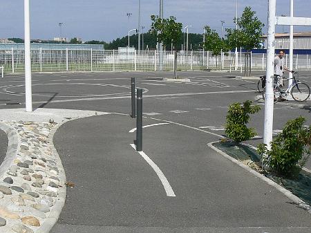 P1070573.JPG - Ces poteaux au milieu de la piste sont dangereux, notamment pour les vélos remontant vers le rond-point des aérostiers. Le franchissement de la chaussée est peu matérialisé. Un trottoir en bord de piste complique la circulation.